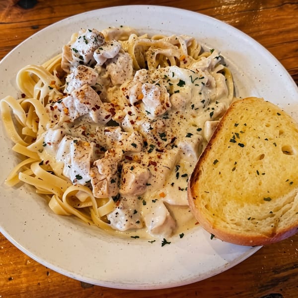 Creamy chicken alfredo pasta with herbs and spices, served with a side of garlic bread.