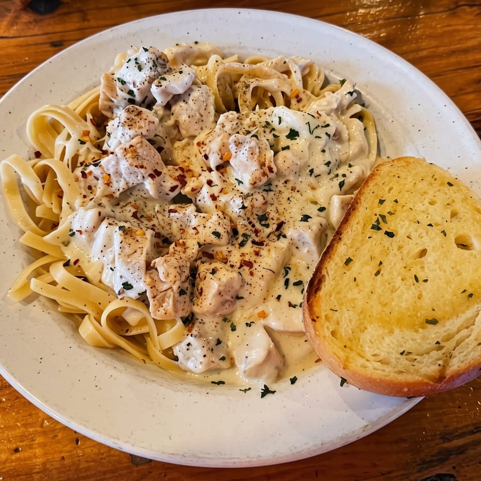 Creamy chicken alfredo pasta with herbs and spices, served with a side of garlic bread.