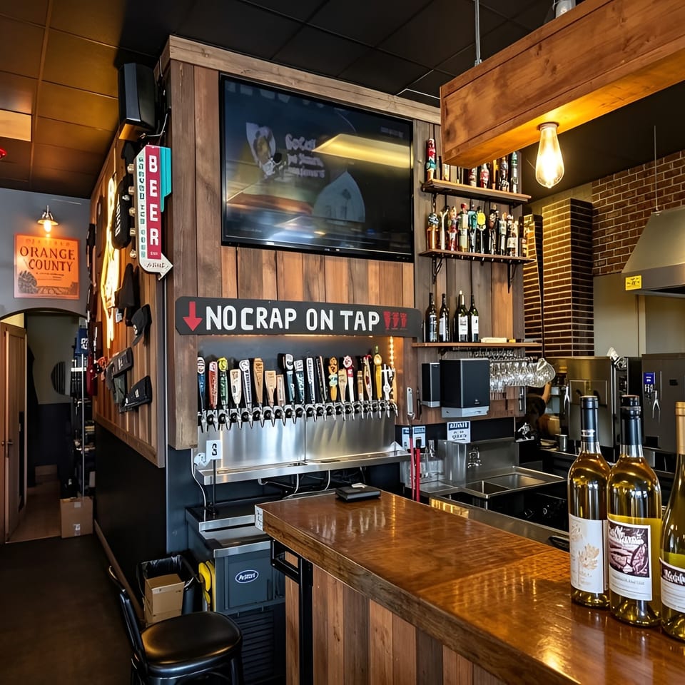 A rustic bar with a wooden counter, beer taps, wine bottles, and a TV screen.