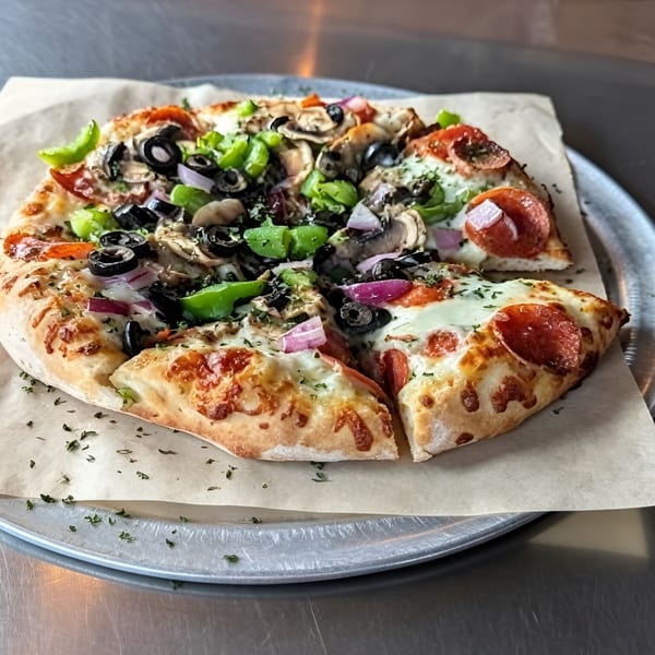 A whole pizza with pepperoni, green peppers, black olives, red onions, and mushrooms on a metal tray.