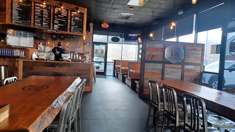 Interior of a TK Pizza and Pasta restaurant with wooden tables, booths, and a counter with a worker.