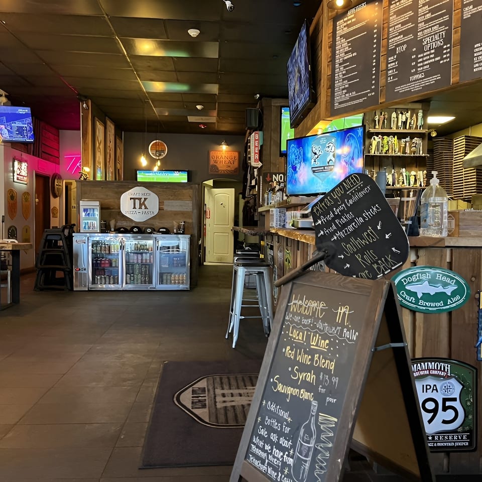 Interior view of a casual restaurant with a bar, menu boards, TVs, and seating areas.