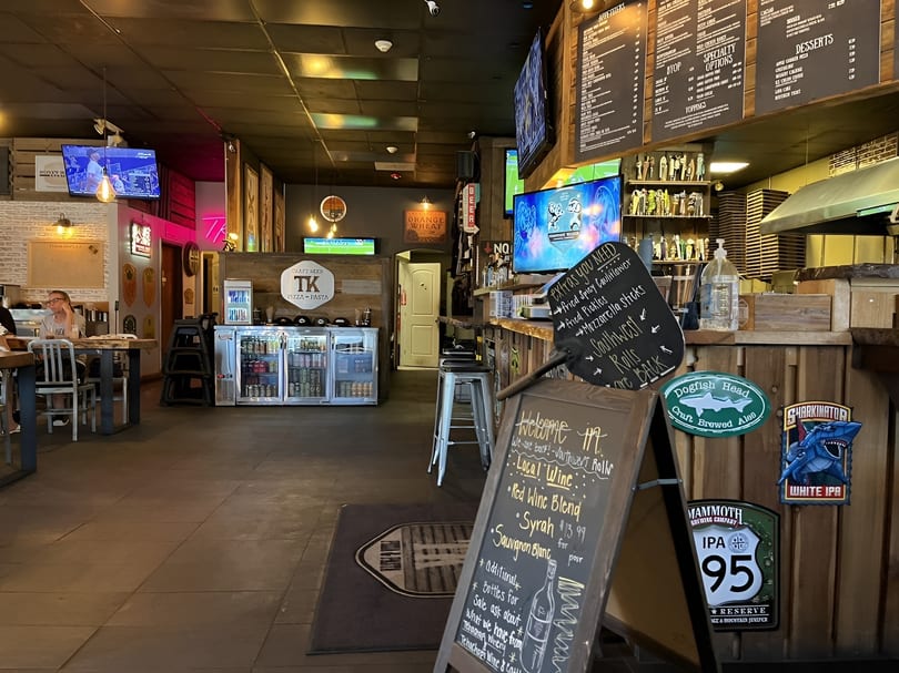 Interior view of a casual restaurant with a bar, menu boards, TVs, and seating areas.